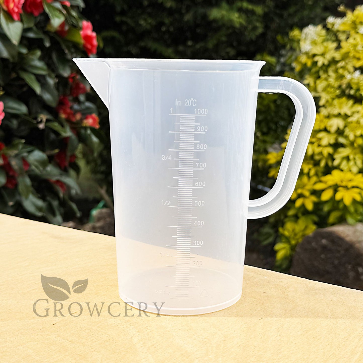 1L measuring jug on table – transparent plastic liquid measure with printed scale and sturdy handle, ideal for gardening or cooking