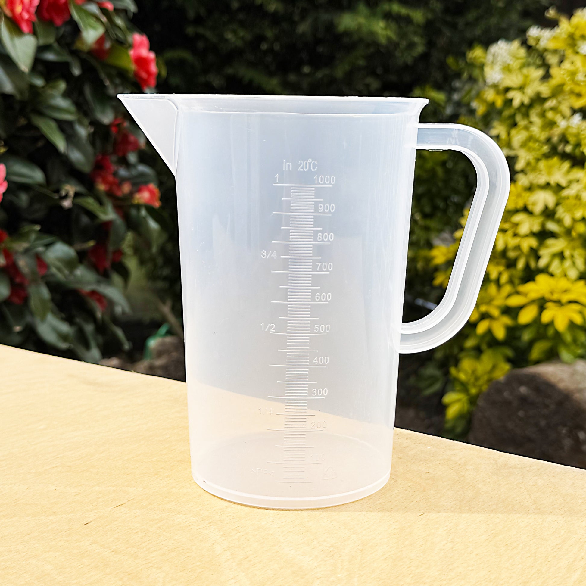 1L measuring jug on table – transparent plastic liquid measure with printed scale and sturdy handle, ideal for gardening or cooking