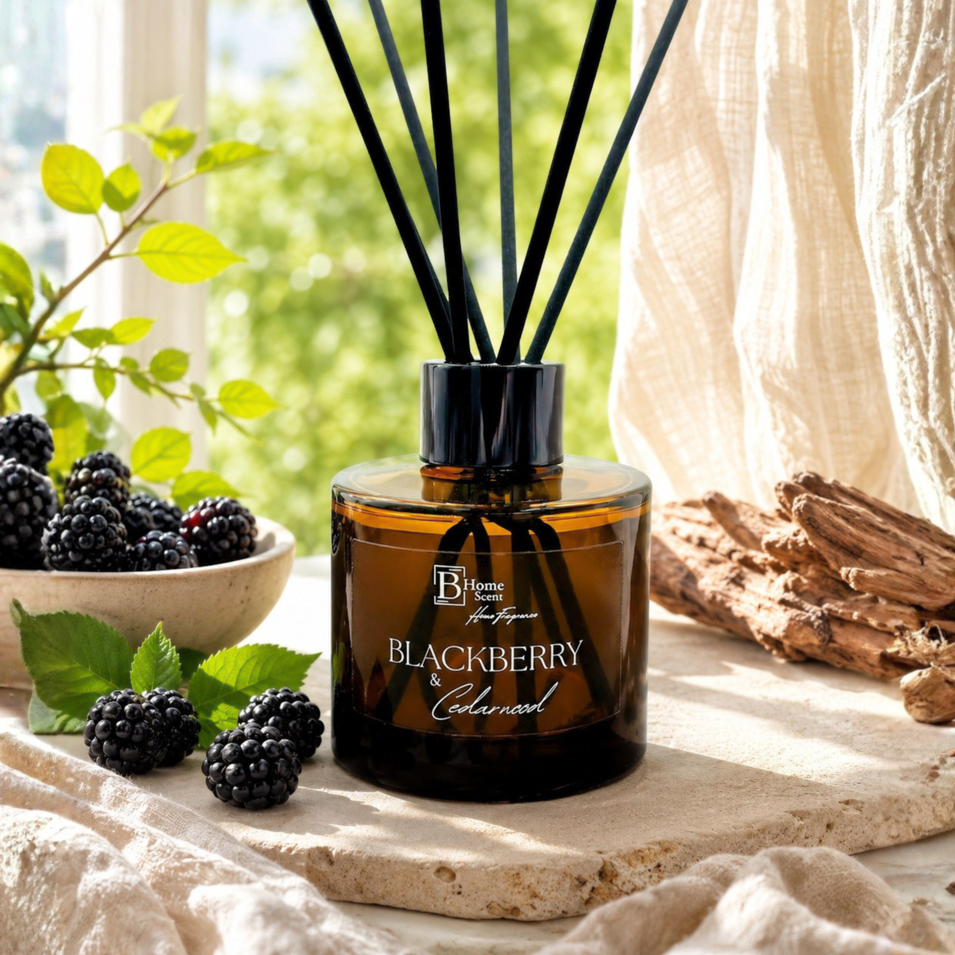 A bottle of Blackberry & Cedarwood reed diffuser on a table with blackberries and greenery.