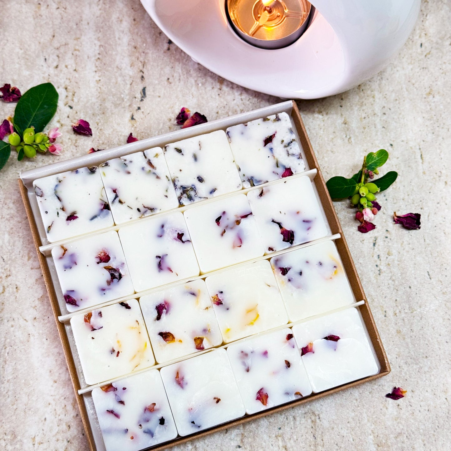 Box of Clean and fresh wax melt collection with floral pieces on a light surface with a candle in the background.