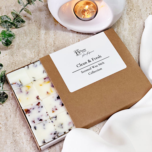 Box of Clean and fresh wax melt collection with a lit candle in the background