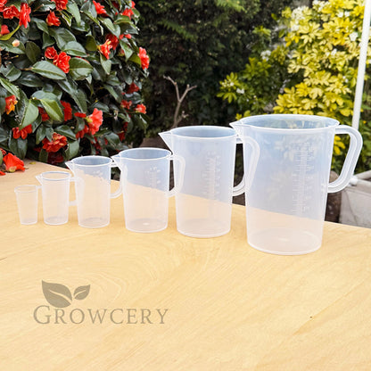 Plastic measuring jug set – sizes from 50ml to 5L lined up on wooden surface with garden background, ideal for gardening, baking, and DIY