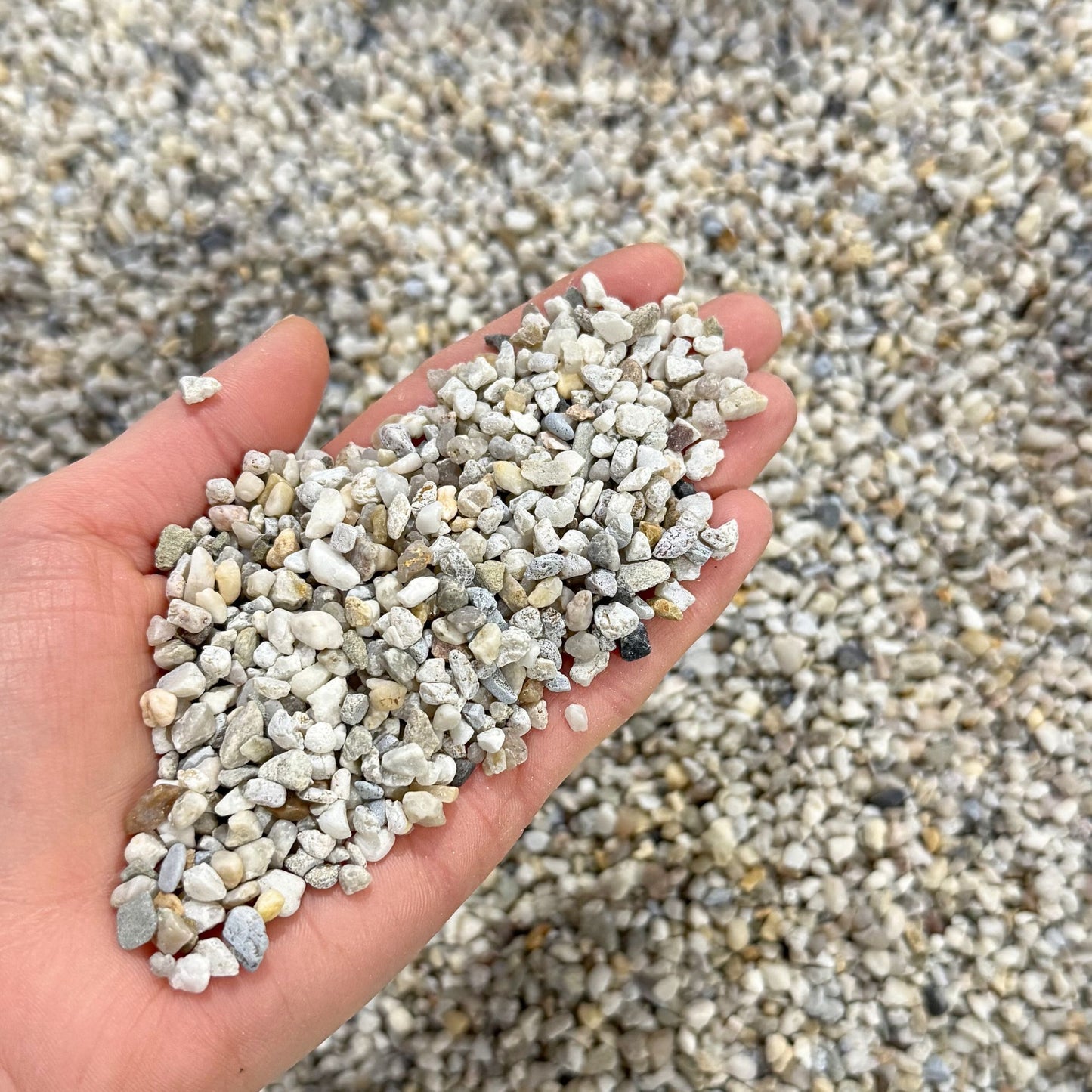 Close-up of natural 3–5mm aquarium gravel held in hand showing rounded quartz stones suitable for fish tank substrate and aqua scaping.